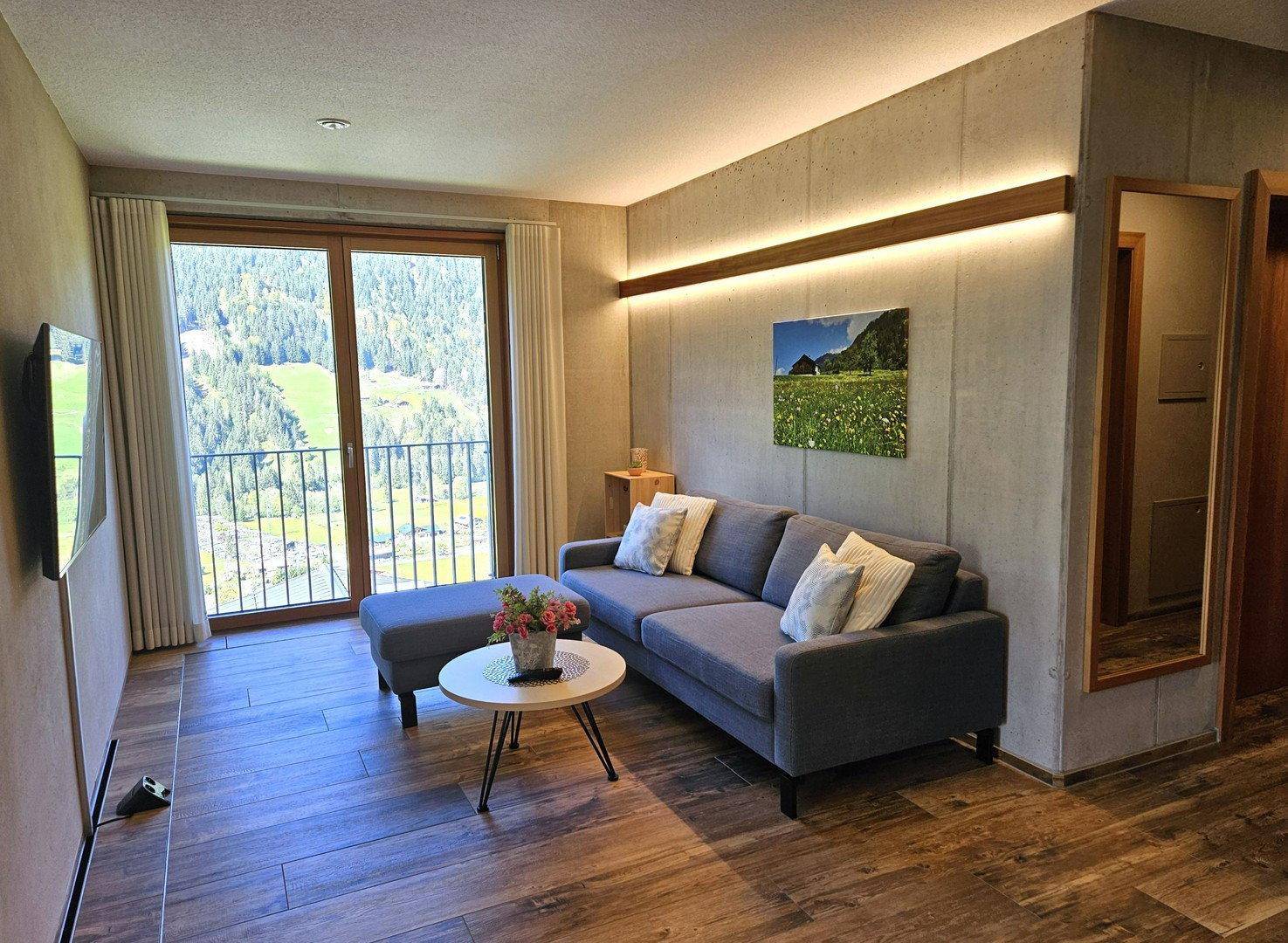 Helles Wohnzimmer mit Holzboden, modernem Sofa und Zugang zu einem Balkon mit Bergblick.