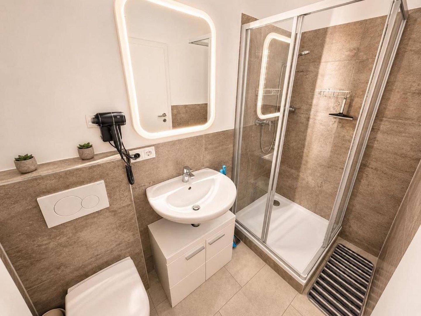 Modernes Badezimmer mit Duschkabine, Waschbecken und beleuchtetem Spiegel.