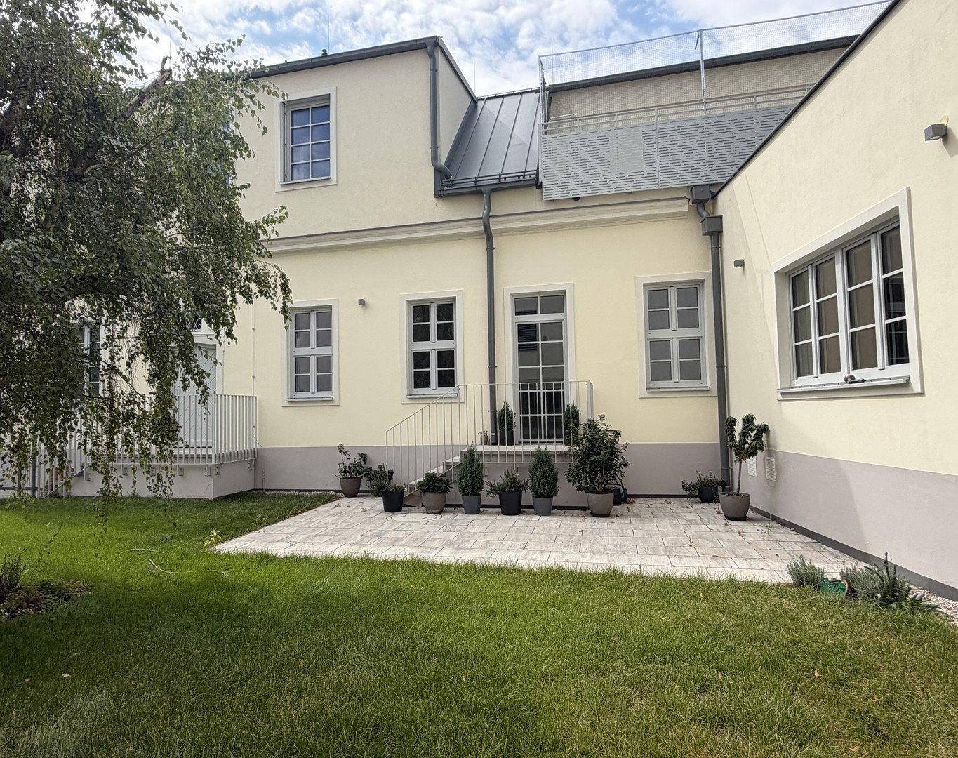 Gepflegter Gartenbereich mit Rasen und gepflasterter Terrasse hinter dem Gebäude.
