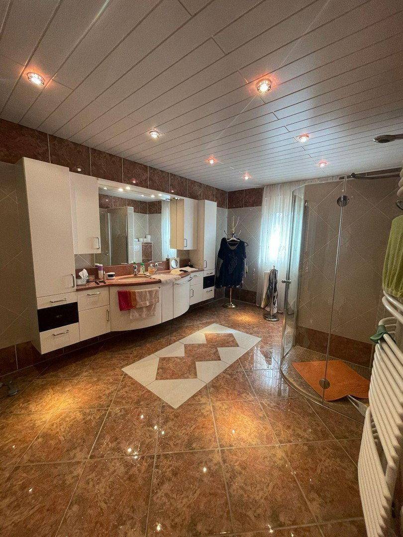 Geräumiges Badezimmer mit Doppelwaschbecken, Duschkabine und braunen Fliesen.