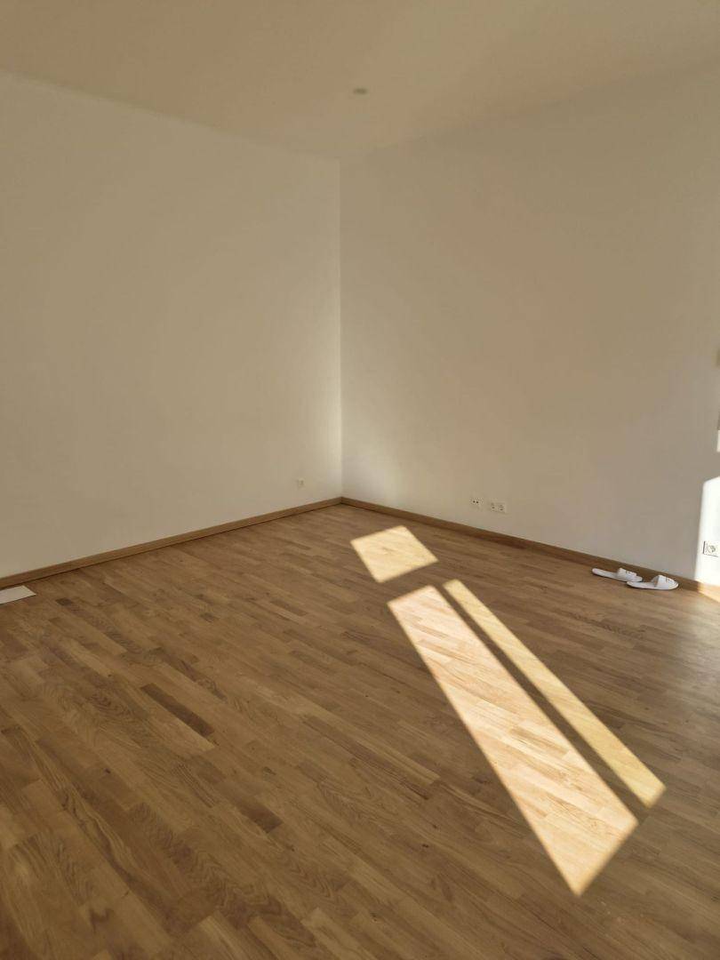 Leerer, heller Raum mit Holzboden und Sonnenlicht, das durch ein Fenster fällt.