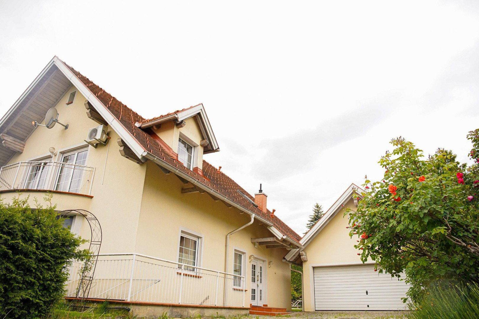 Ansicht des Hauses mit Satteldach, Balkon und einer integrierten Garage, umgeben von Grün.