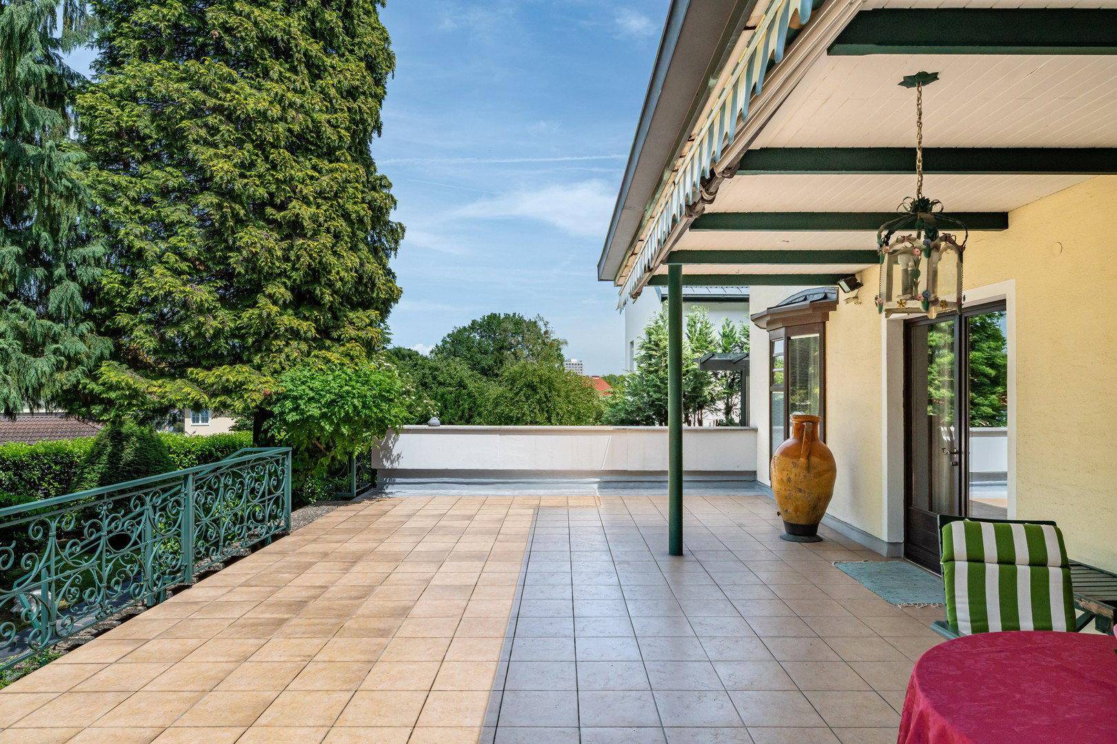 Große geflieste Terrasse mit schmiedeeisernem Geländer und weitem Blick ins Grüne.