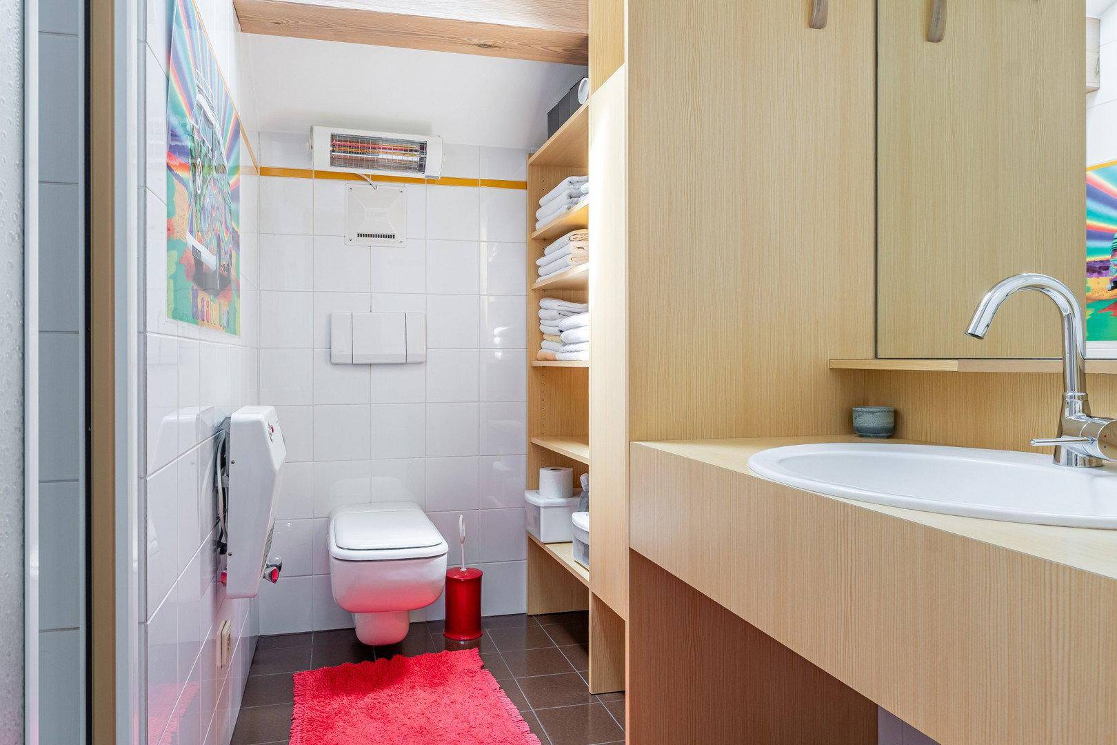 Funktionales Badezimmer mit WC, Waschbecken und Holzregalen für Handtücher.