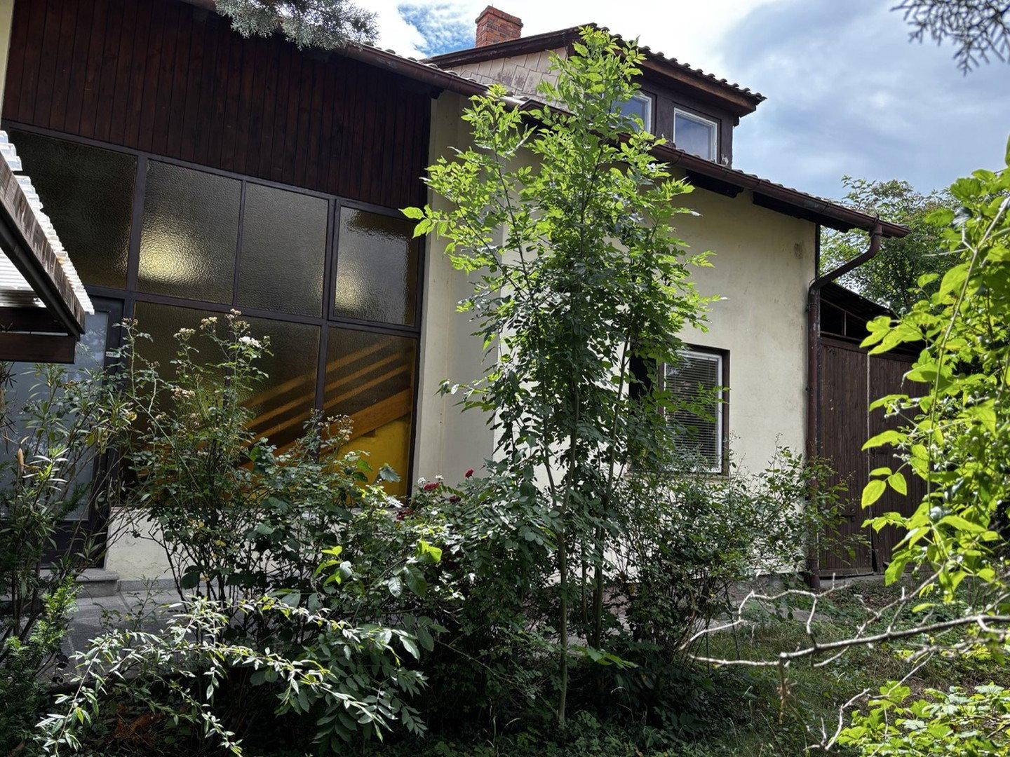 Seitenansicht des Hauses mit großen Fenstern und üppiger Vegetation.