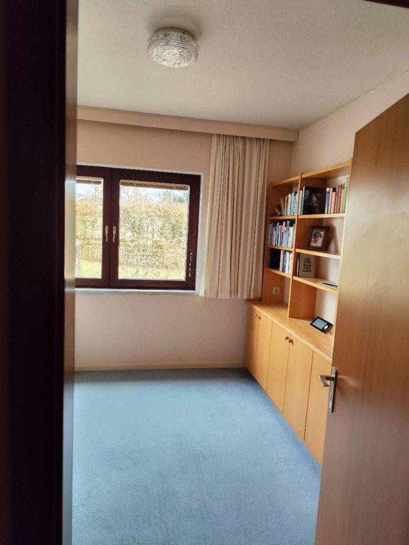 Arbeitszimmer mit blauem Teppichboden, Holzschränken und Fenster.
