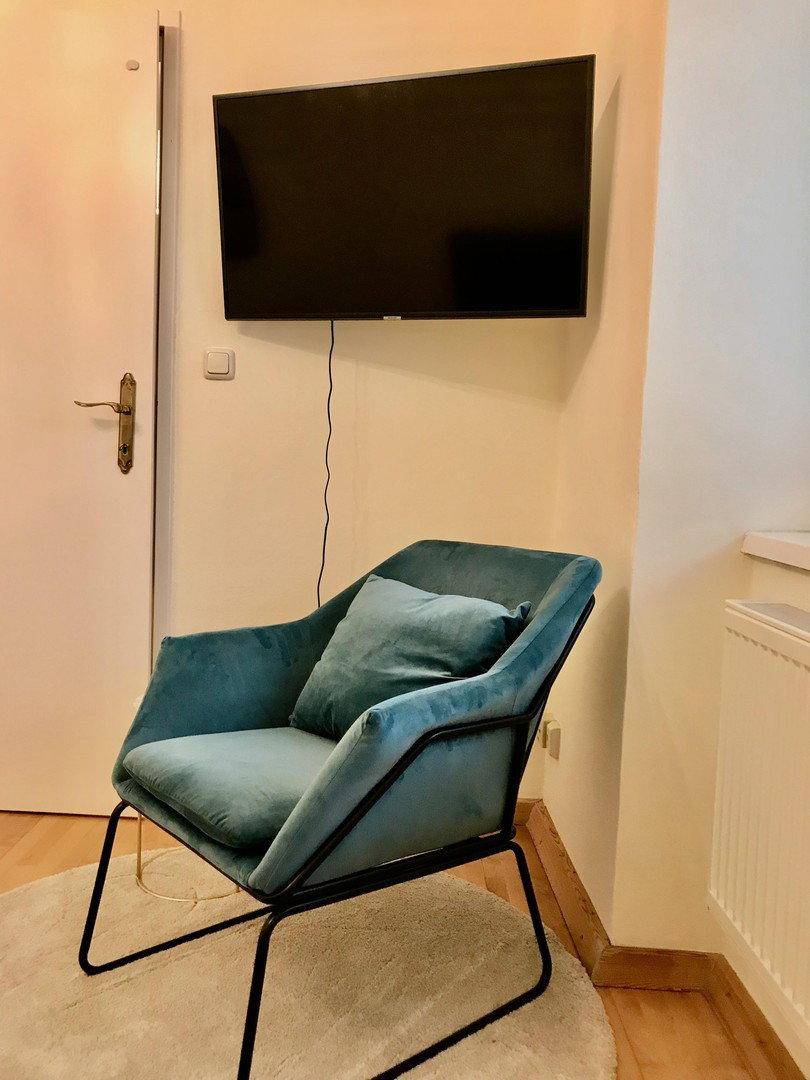 Nahaufnahme des tealfarbenen Sessels und des Wandfernsehers im Schlafzimmer.