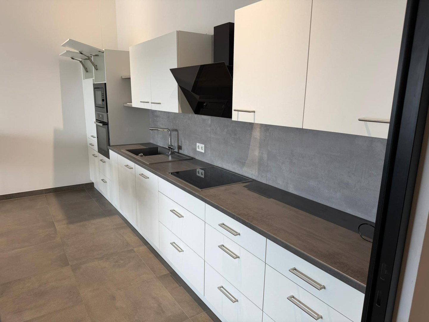 Moderne Einbauküche mit weißen Schränken, dunkler Arbeitsplatte und integrierten Geräten.