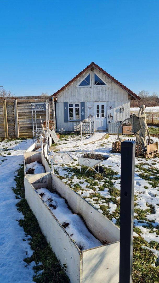 Kleines Gartenhaus in einem verschneiten Gartenbereich mit Hochbeet und ländlicher Umgebung.