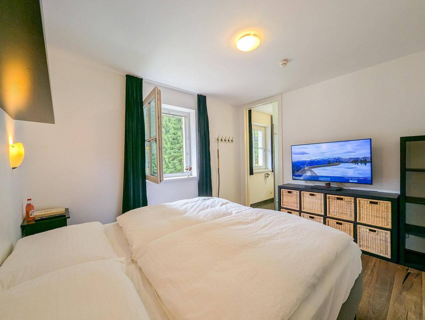 Schlafzimmer mit Doppelbett, Fernseher und Fenster mit Blick ins Grüne.