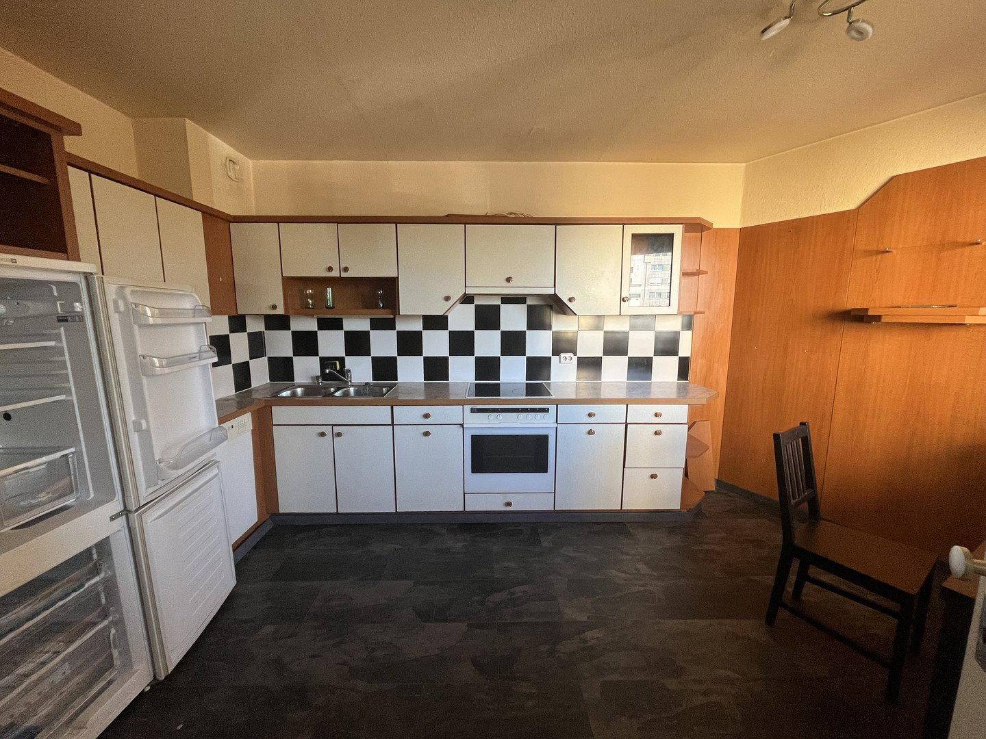 Küche mit weißen Schränken, Holzdetails, schwarz-weiß gefliester Rückwand und Kühlschrank.