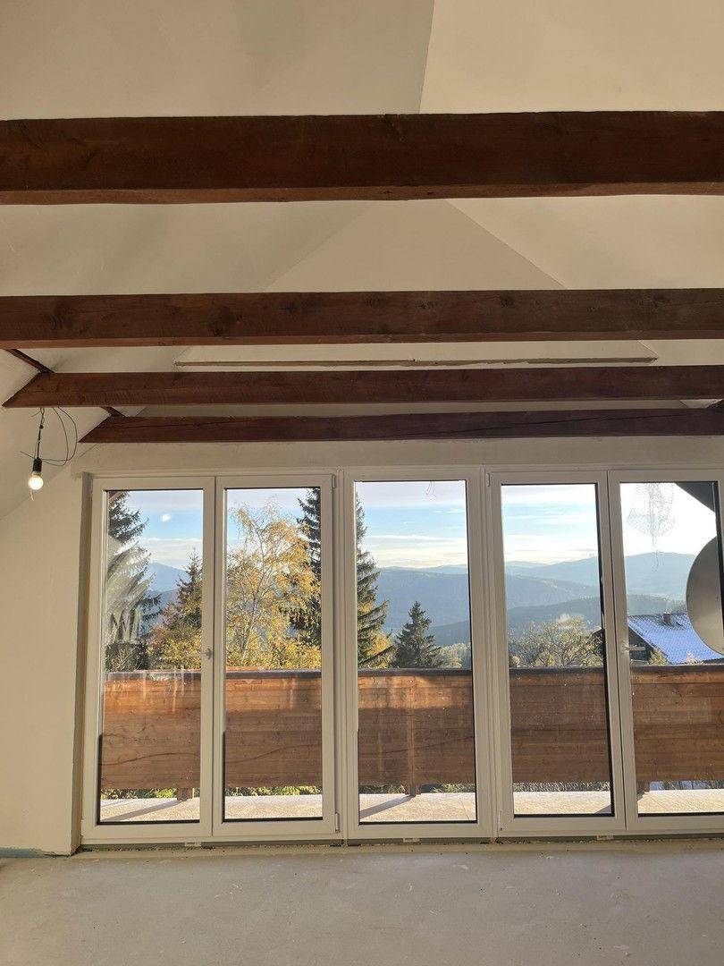 Heller Raum im Dachgeschoss mit großen Fenstern, Holzbalken und Bergblick.