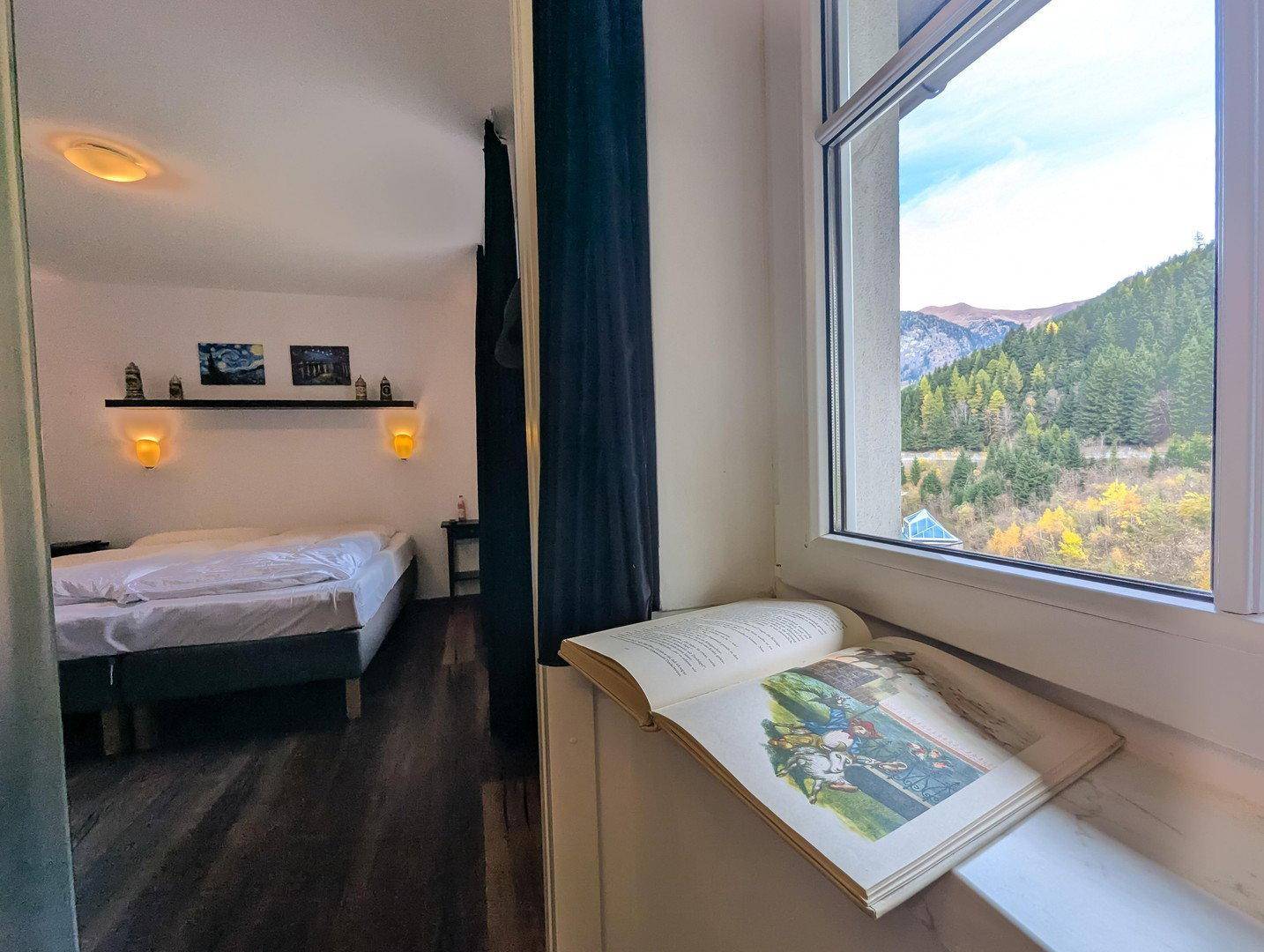 Gemütliches Schlafzimmer mit Blick auf die herbstliche Berglandschaft durch das Fenster.