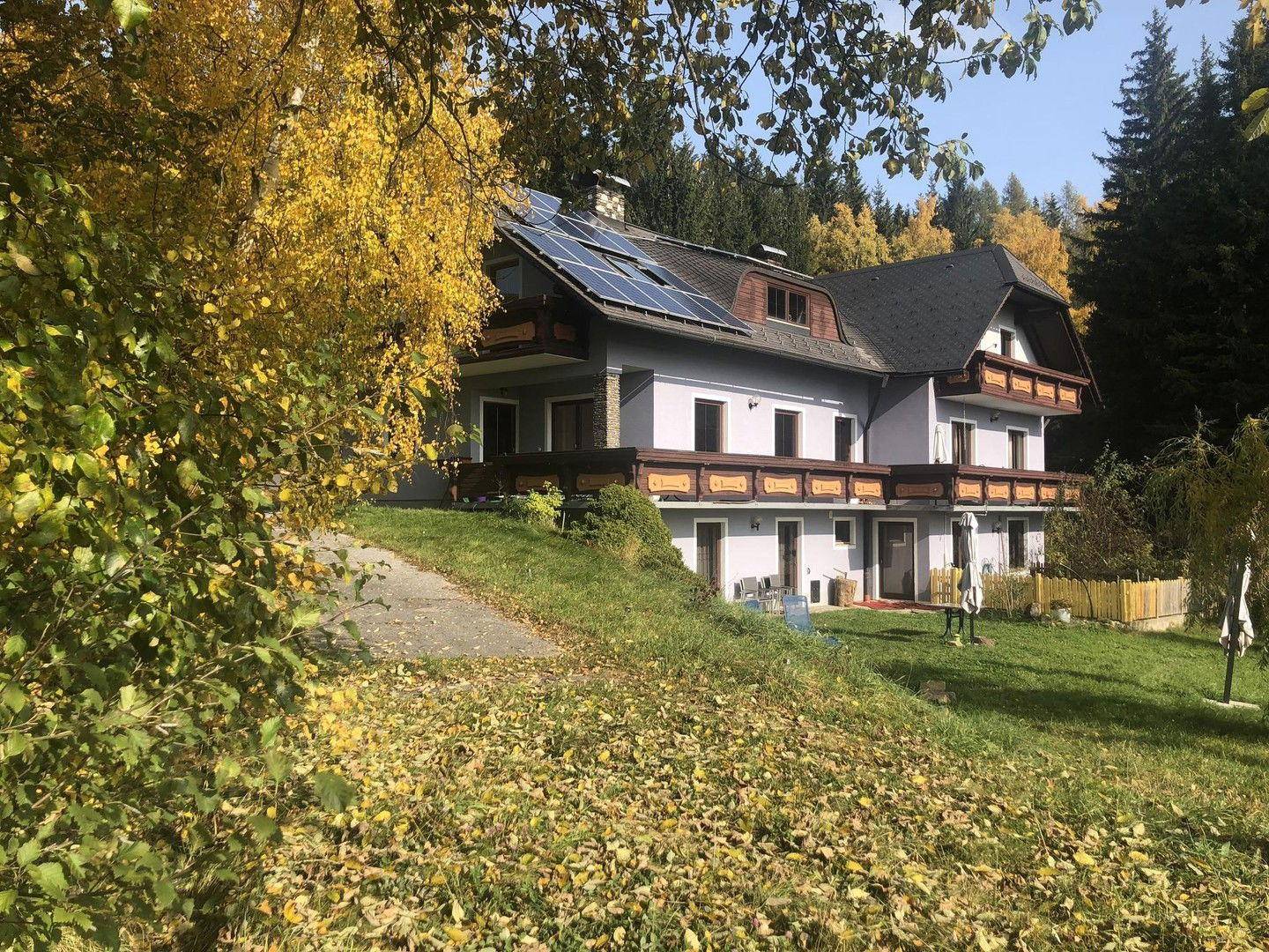 Haus im Herbst mit gelben Blättern, Photovoltaikanlage und grüner Umgebung.