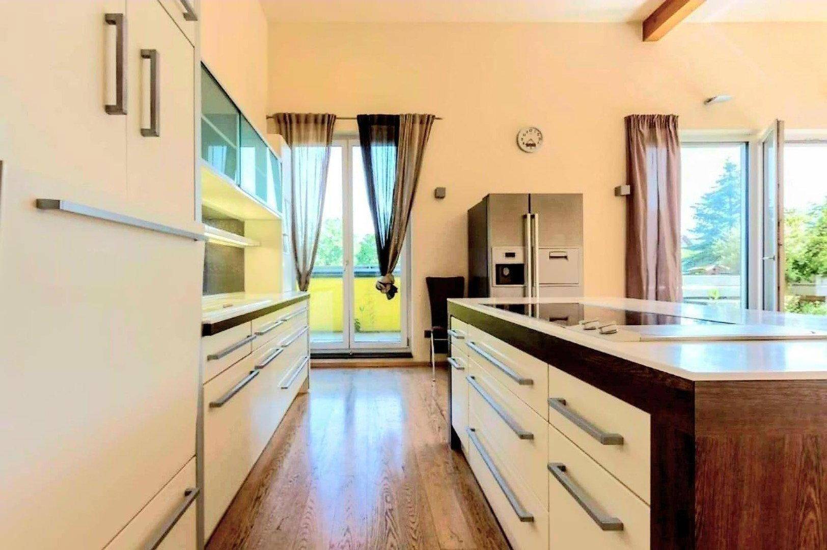Moderne Küche mit weißen Schränken, Kochinsel und Zugang zu einem Balkon.