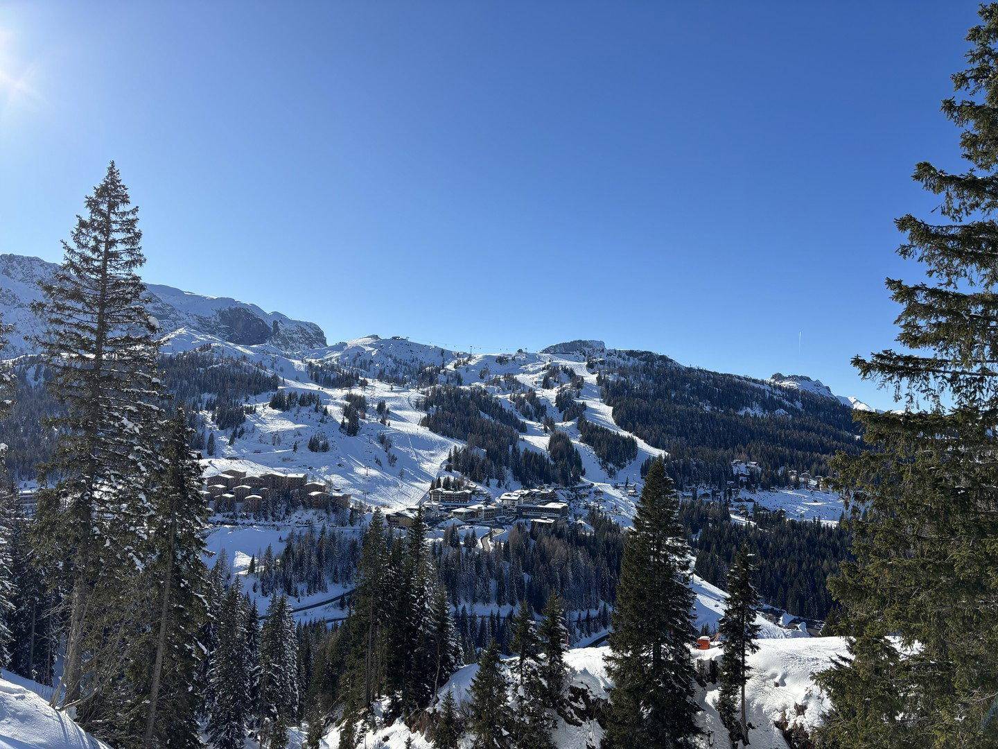Panoramablick auf eine schneebedeckte Berglandschaft mit Skipisten und einem Dorf im Winter.