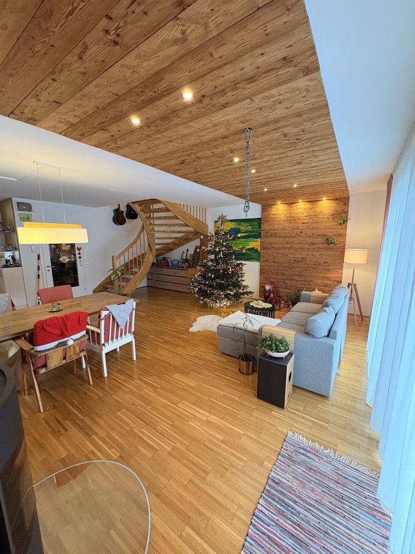 Geräumiger Wohn-Essbereich mit Holzboden, Holzdecke und einer geschwungenen Holztreppe.