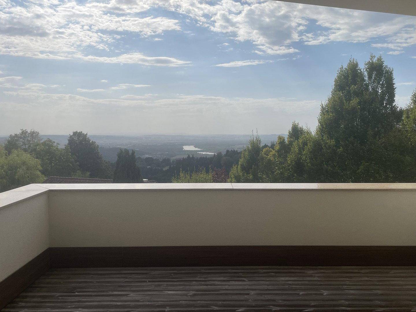 Weitläufiger Ausblick von einem Balkon über eine grüne Landschaft mit einem See in der Ferne.