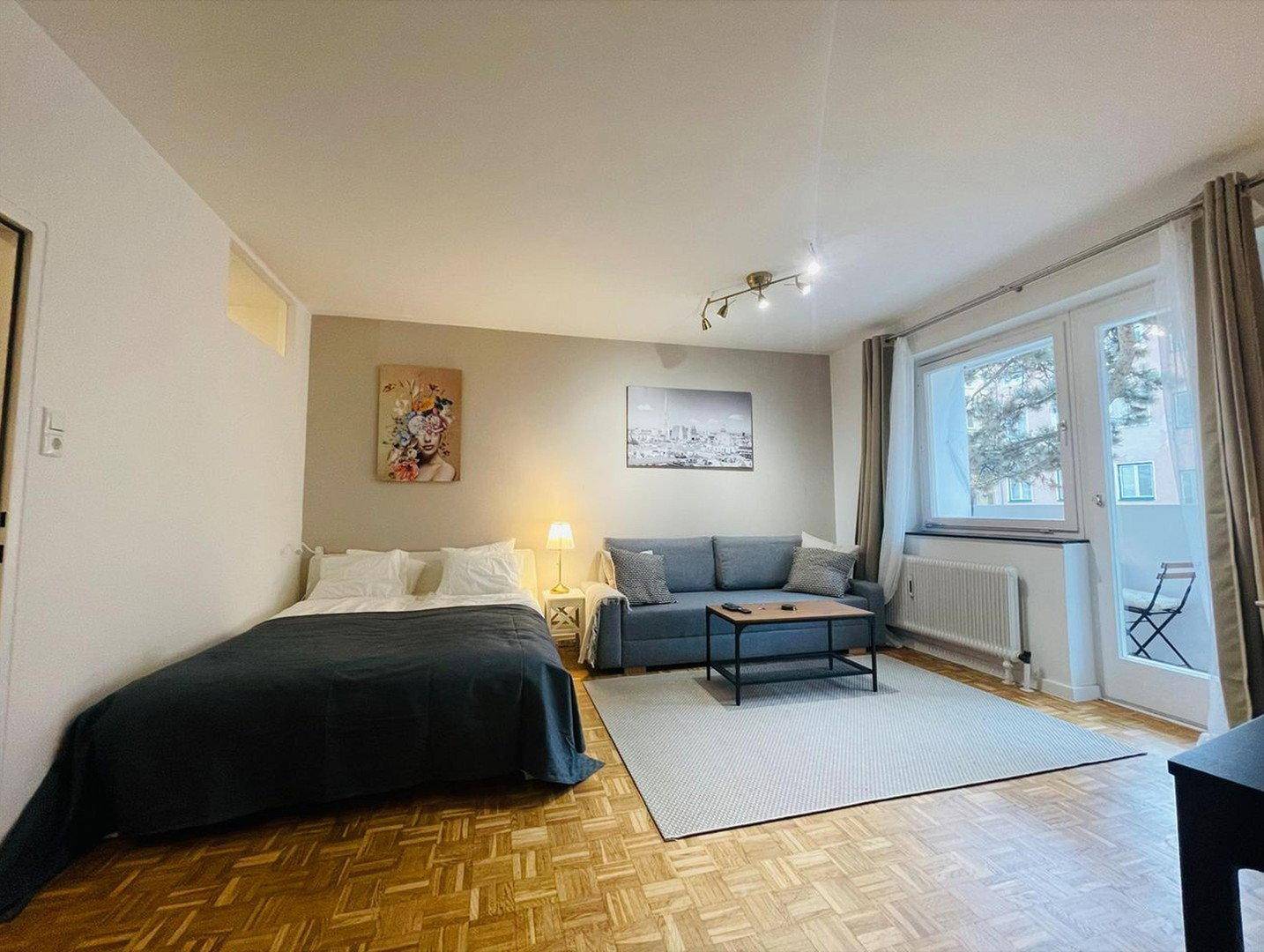 Heller Wohnbereich mit Schlafsofa, Doppelbett und Zugang zu einem kleinen Balkon.