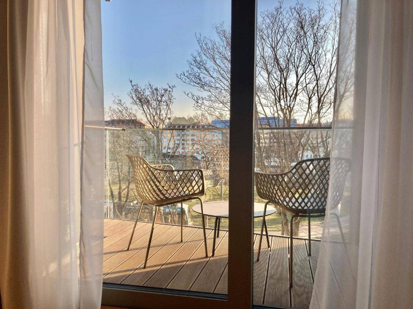 Balkon mit modernen Outdoor-Stühlen und einem kleinen Tisch, umgeben von Bäumen.