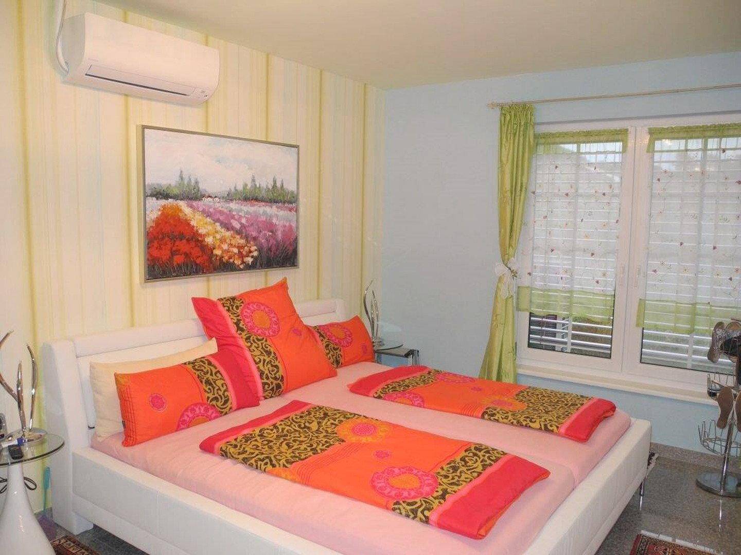 Helles Schlafzimmer mit Doppelbett, farbenfroher Bettwäsche und Klimaanlage.