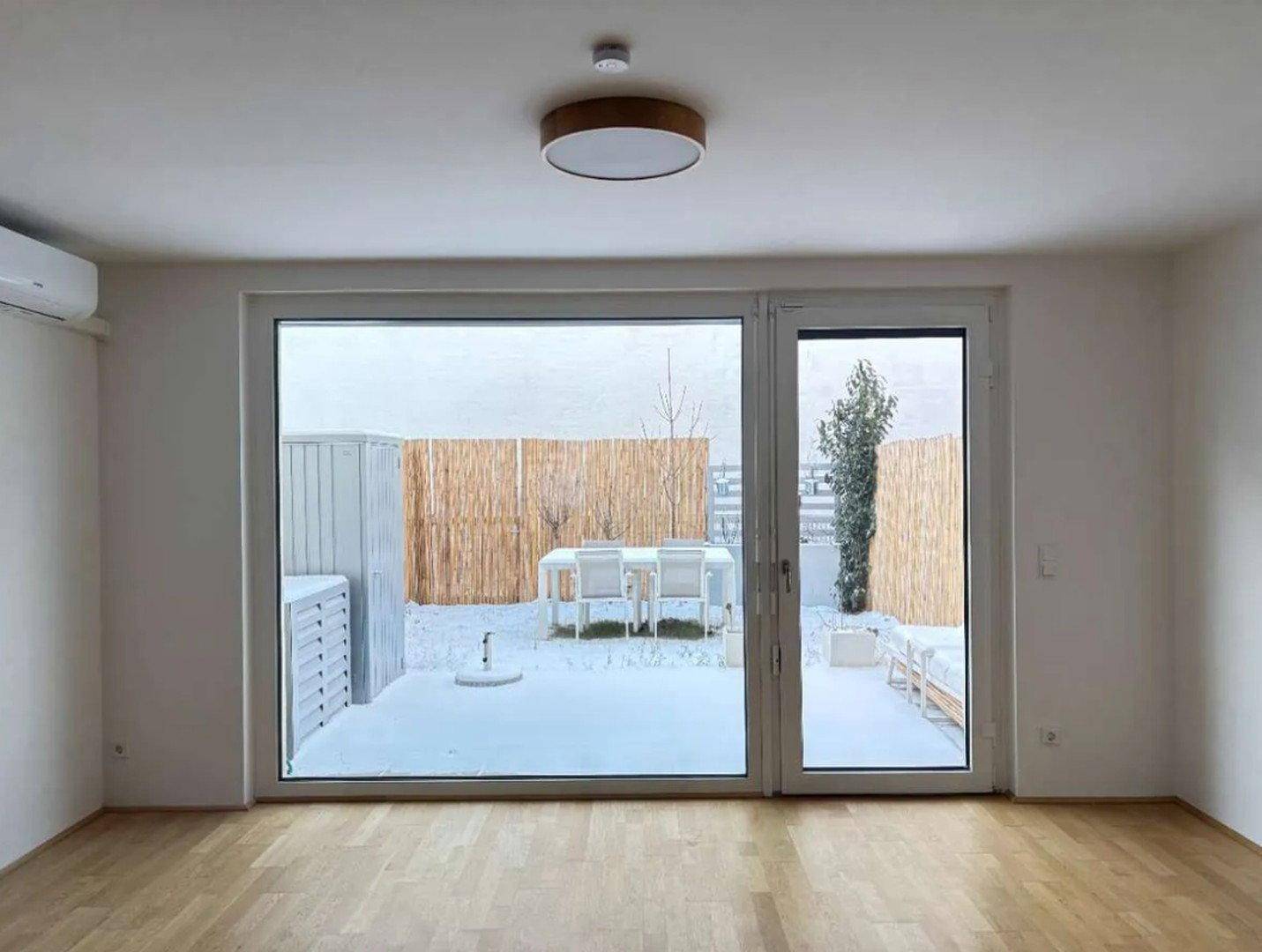 Helles Wohnzimmer mit großen Fenstern und Zugang zu einer schneebedeckten Terrasse mit Sitzgelegenheiten.