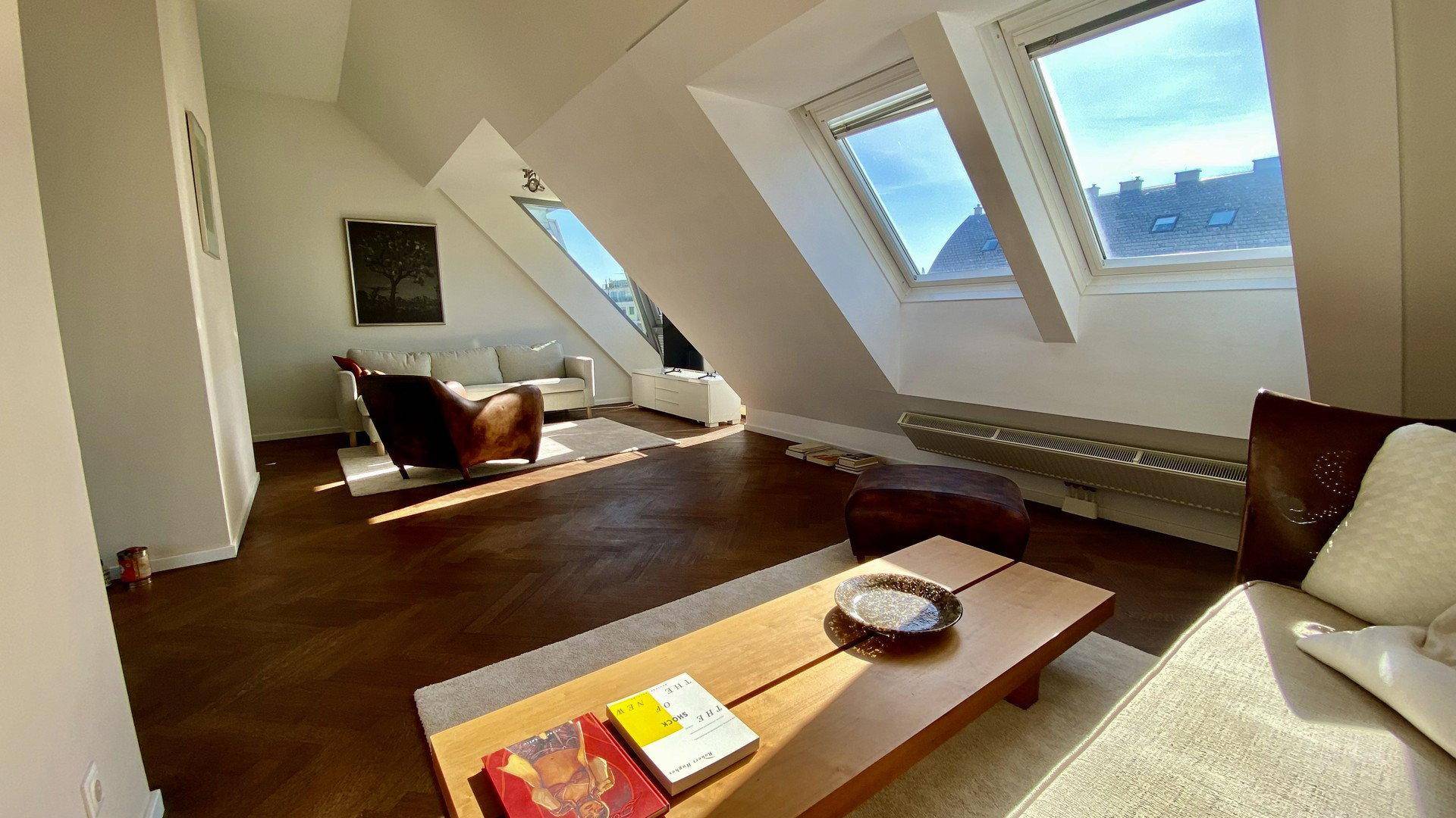 Helles Wohnzimmer mit schrägen Dachfenstern, Holzboden und moderner Einrichtung.
