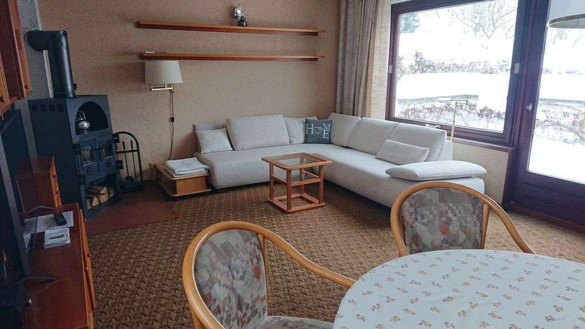 Wohn-Essbereich mit Kaminofen, Sofa und Blick auf die verschneite Landschaft.