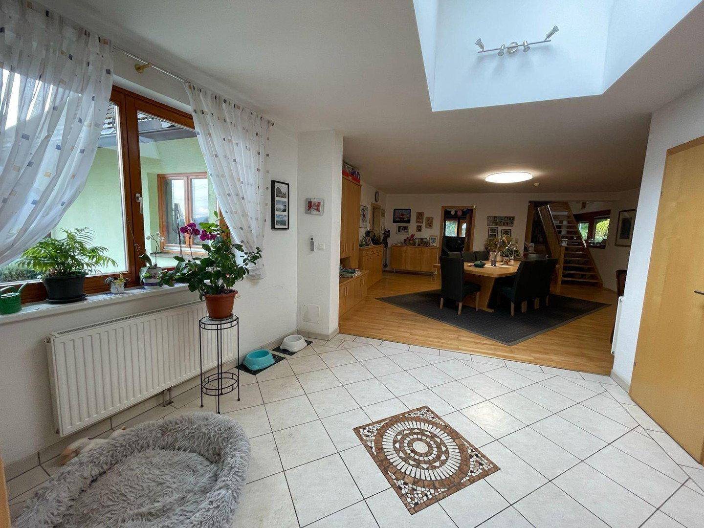 Offener Wohn- und Essbereich mit Fliesenboden, großem Fenster und Blick in den Garten.