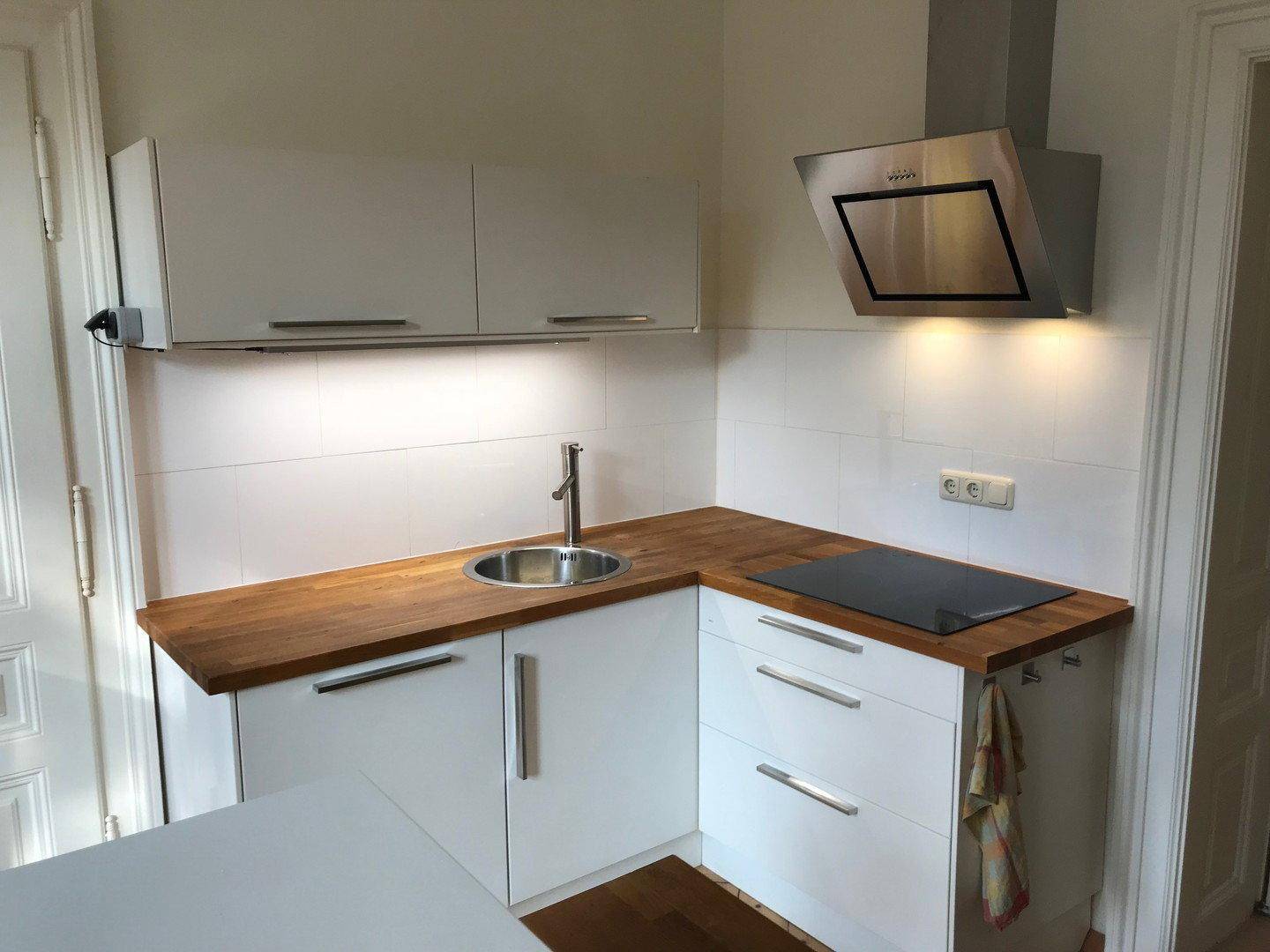 Moderne Einbauküche mit weißen Schränken, Holz-Arbeitsplatte, Spüle und Induktionskochfeld mit Dunstabzugshaube.