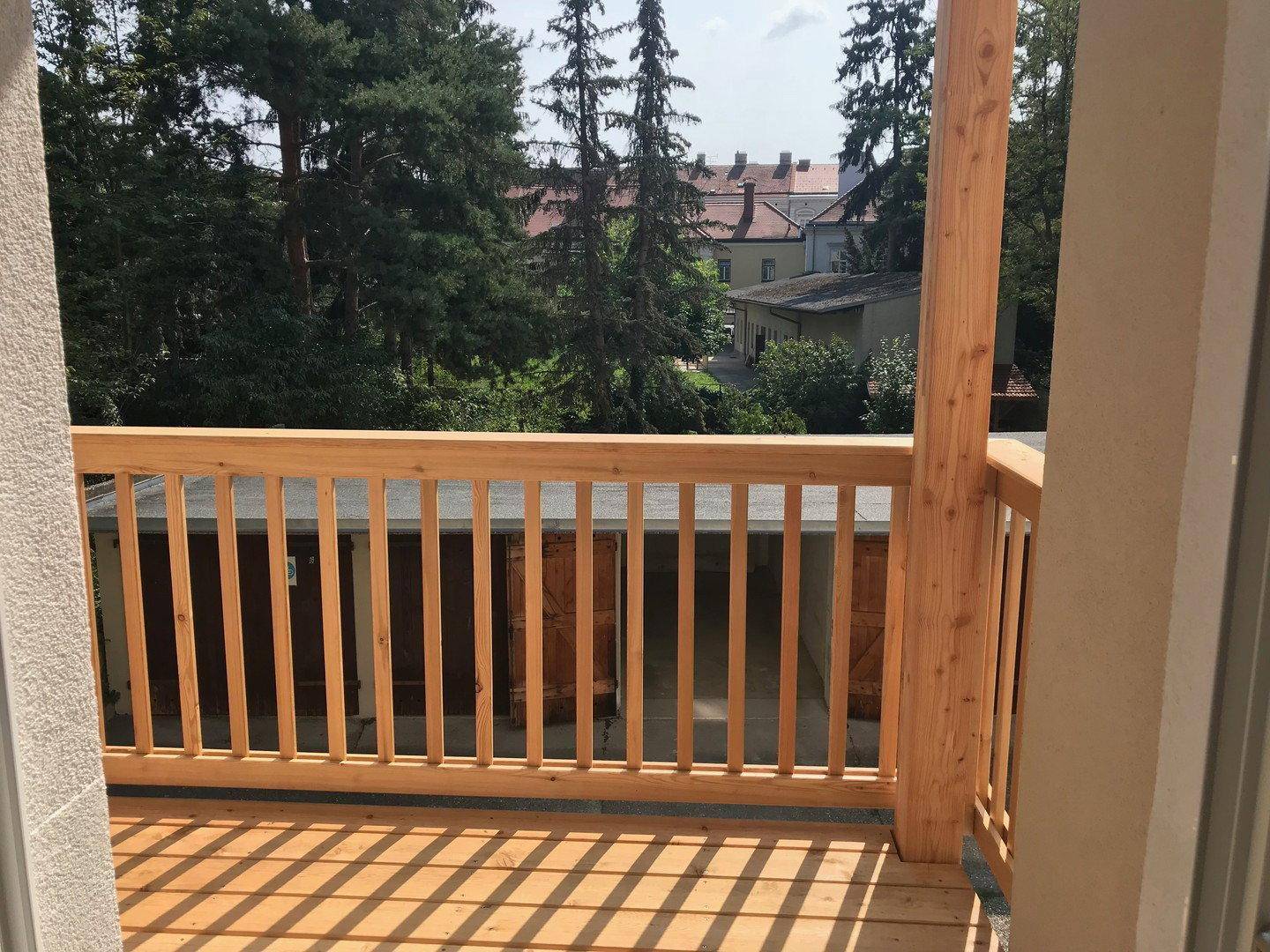 Balkon mit Holzgeländer und Blick auf Garagen sowie eine grüne Umgebung mit Bäumen.
