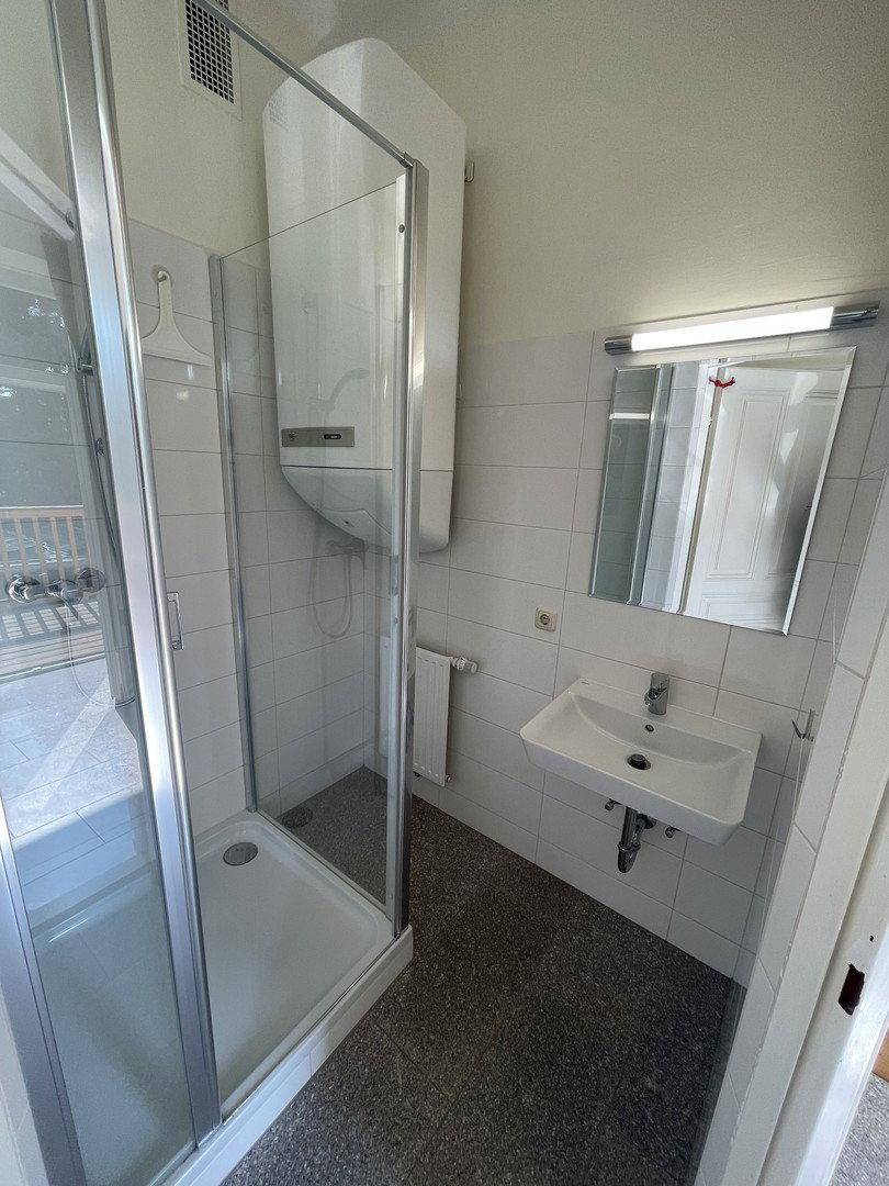 Kompaktes Badezimmer mit Duschkabine, Waschbecken, Spiegel und Handtuchheizkörper.