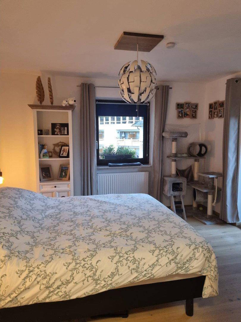 Schlafzimmer mit Doppelbett, Fenster und Bücherregal, Holzboden und helle Wände.