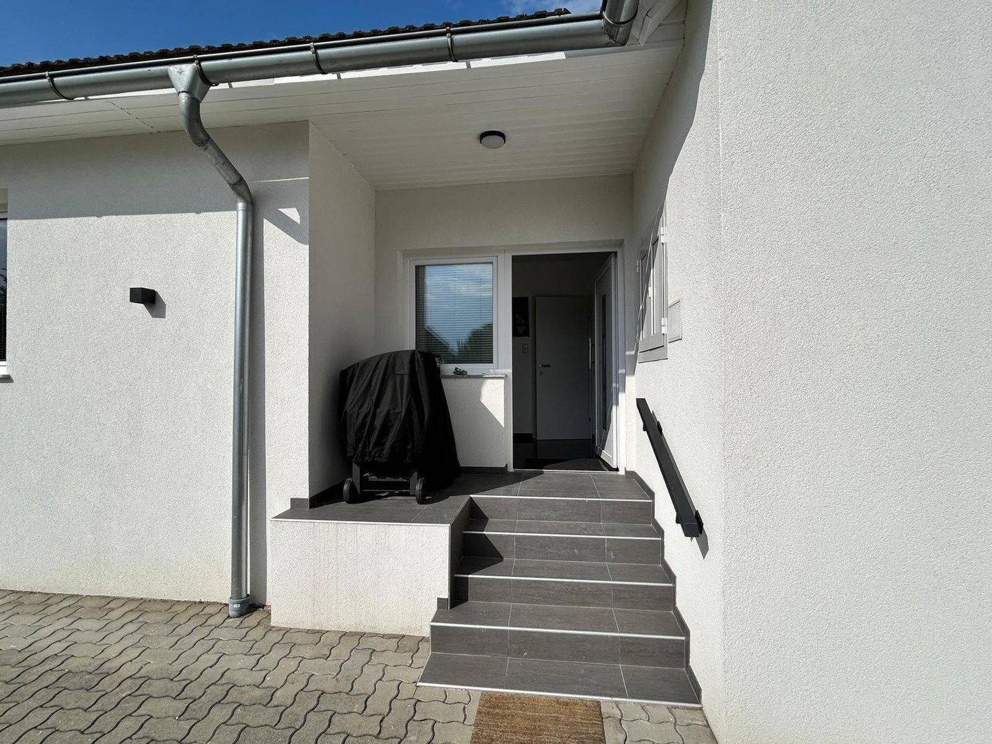 Eingangsbereich des Hauses mit Treppe, Grill und moderner Fassadengestaltung.