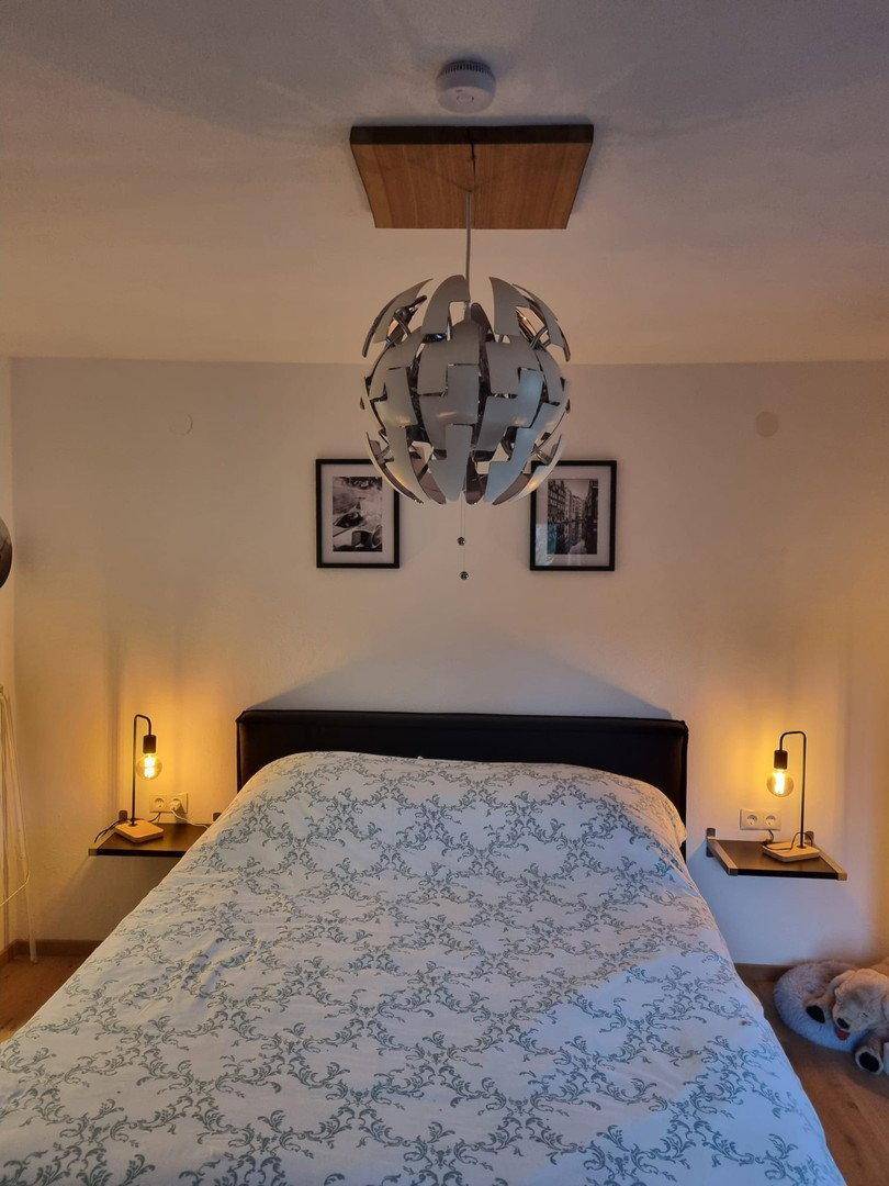 Schlafzimmer mit Doppelbett, Nachttischen und moderner Deckenleuchte, Holzboden.
