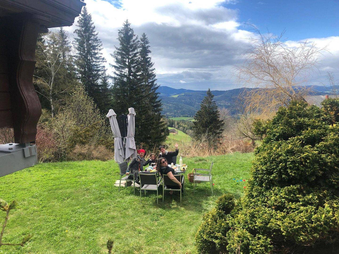 Familie genießt ein Essen im Garten mit Bergblick unter blauem Himmel.
