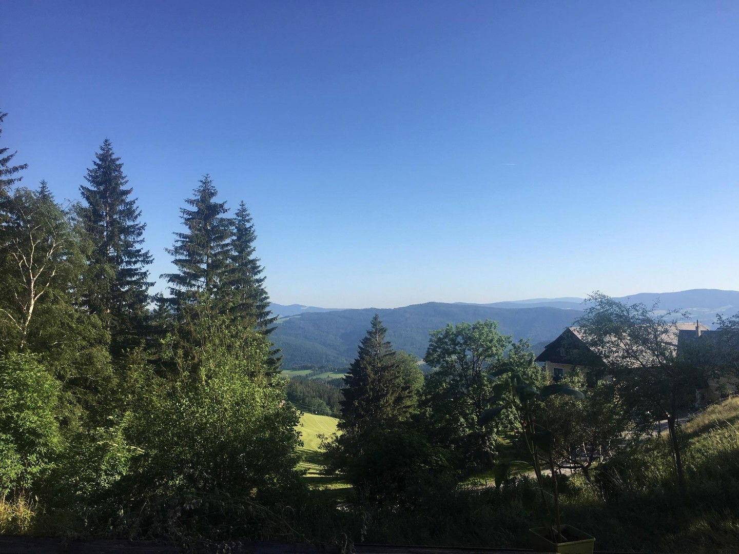 Weitläufige grüne Berglandschaft unter blauem Himmel mit vereinzelten Häusern.