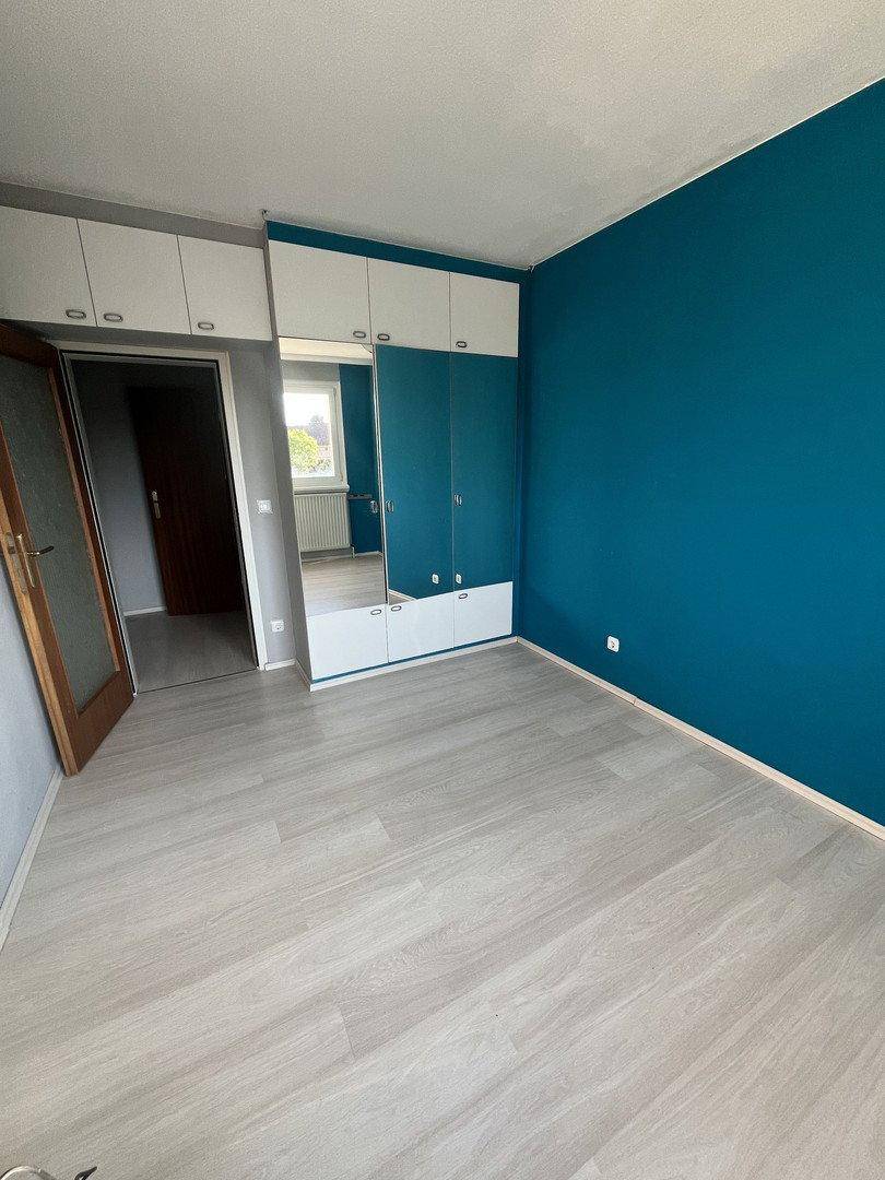 Schlafzimmer mit Laminatboden, blauer Akzentwand und Einbauschränken mit Spiegelfront.