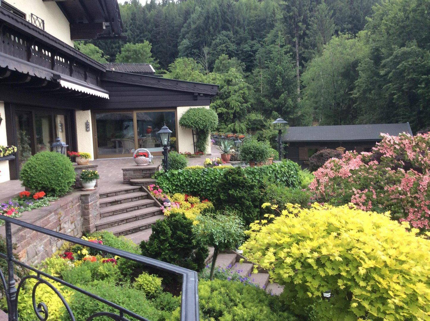 Gepflegter Gartenbereich mit bunten Blumenbeeten, Sträuchern und Steintreppen neben dem Haus.