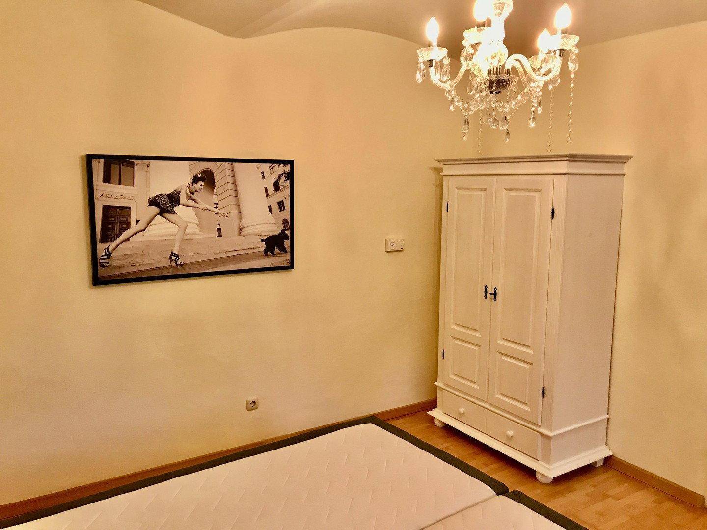 Schlafzimmer mit Bett, weißem Kleiderschrank und dekorativem Wandbild.