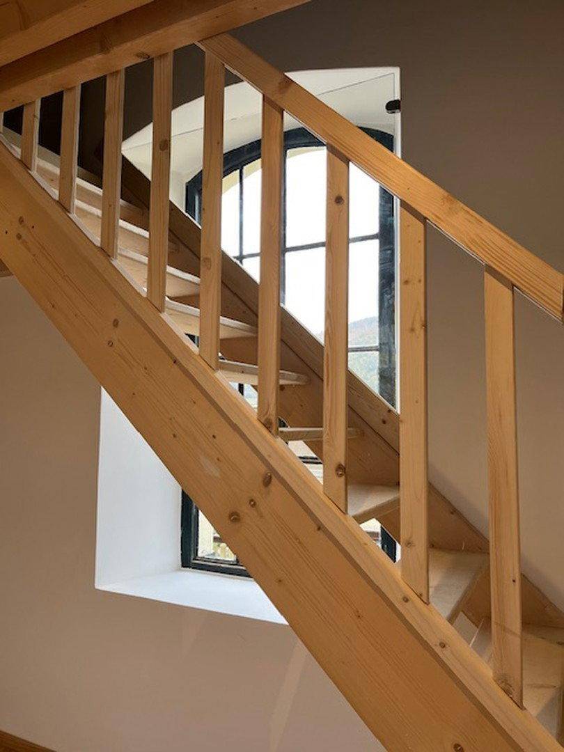 Holztreppe mit Geländer und Fenster, das natürliches Licht in den Treppenbereich bringt.