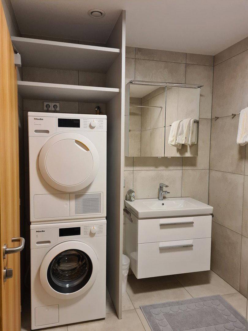 Modernes Badezimmer mit Waschbecken, Spiegelschrank und integrierter Waschmaschine und Trockner.