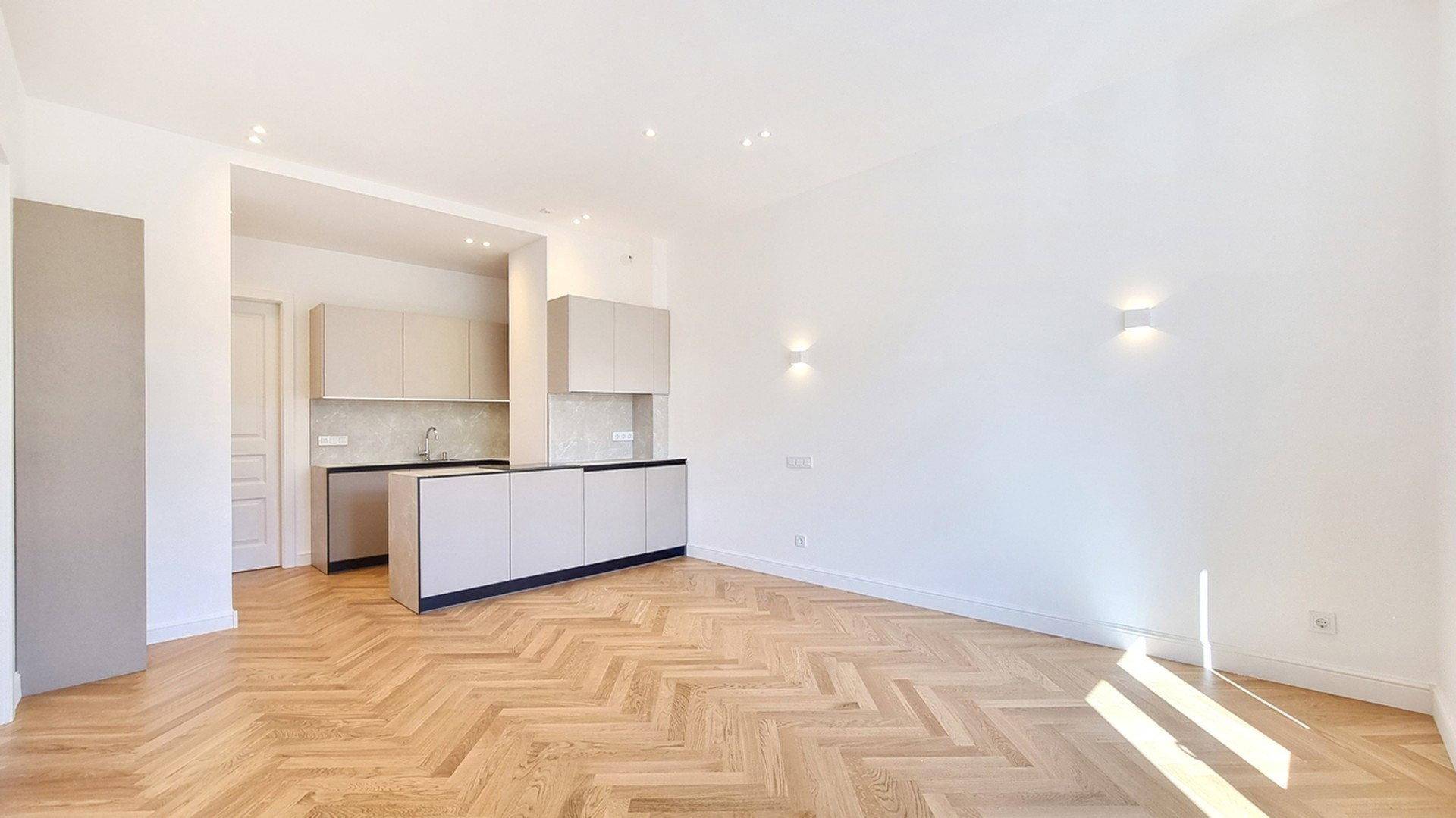 Lichtdurchfluteter Wohnbereich mit moderner Küchenzeile und elegantem Fischgrätparkettboden.