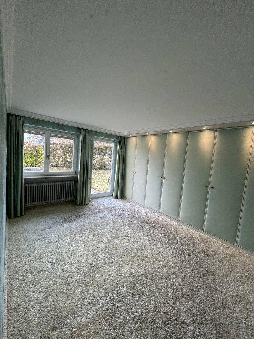 Geräumiges Schlafzimmer mit hellem Teppichboden, Einbauschränken und Blick ins Grüne.