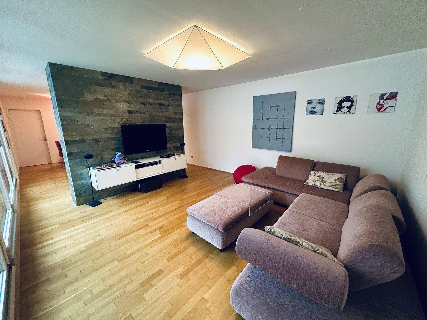 Helles Wohnzimmer mit moderner Steinwand, Fernseher und beigem Ecksofa.