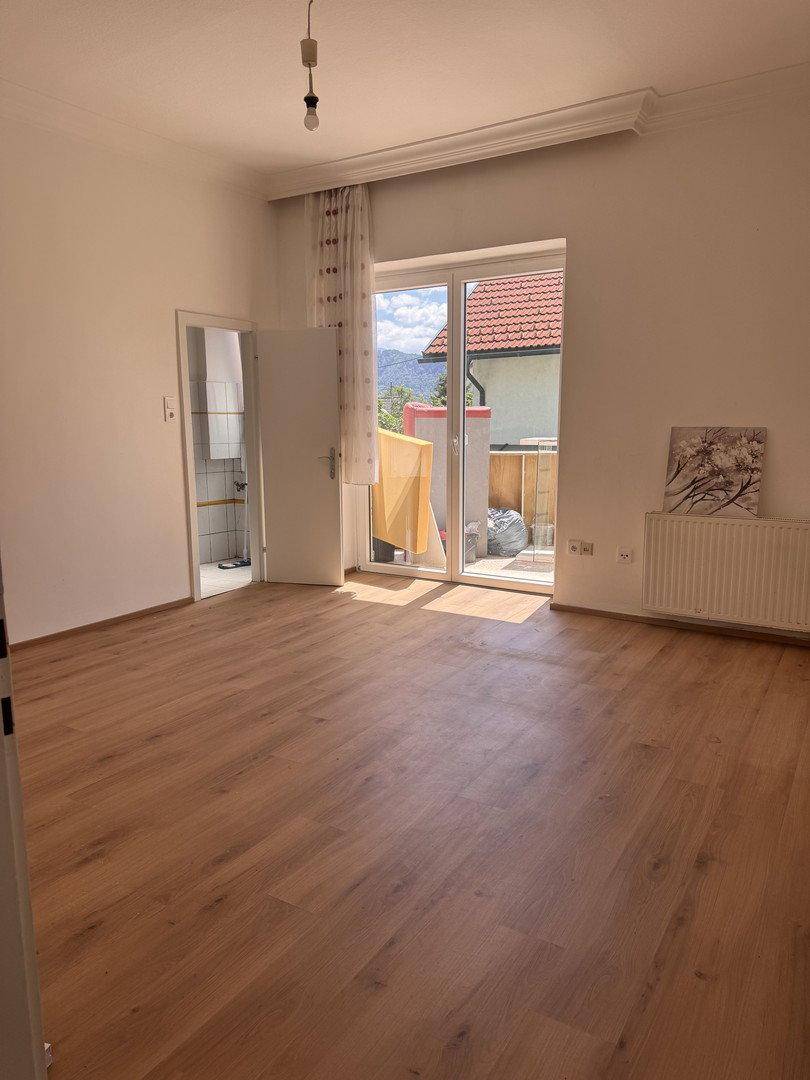 Heller Raum mit Holzboden, Zugang zur Terrasse und Blick auf die umliegende Berglandschaft.