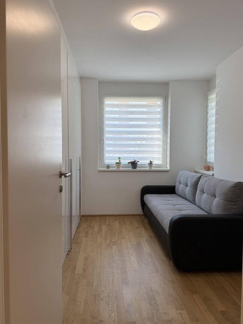 Helles Schlafzimmer mit Schlafsofa, Holzboden und weißen Einbauschränken.