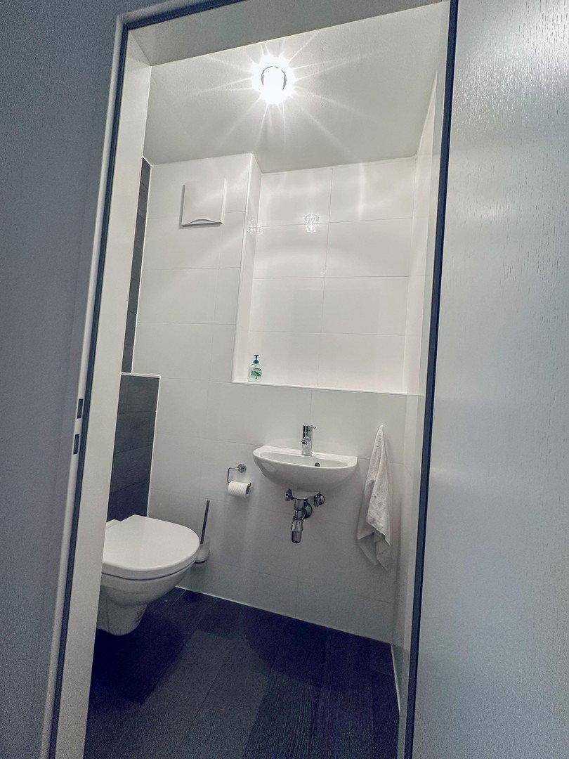 Kleines Gäste-WC mit Wand-WC, Waschbecken und modernen Fliesen.