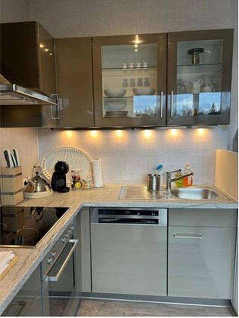 Moderne Küchenzeile mit glänzenden Schränken, Induktionskochfeld, Spülmaschine und Unterbauleuchten.