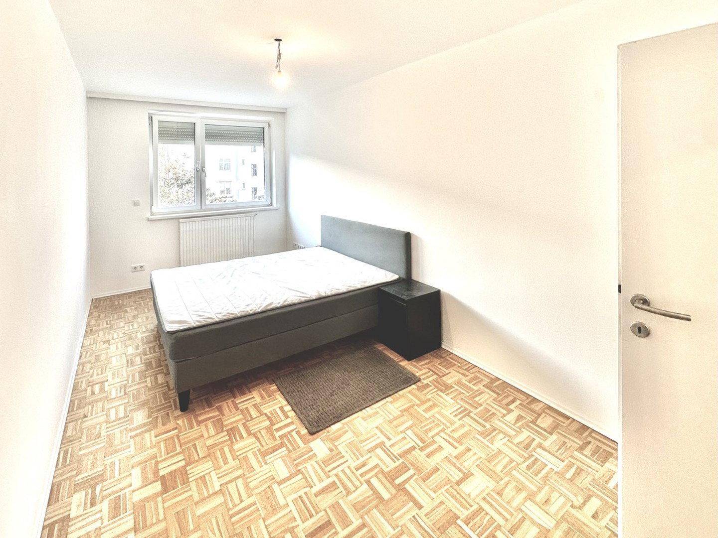 Schlafzimmer mit Parkettboden, einem Bett und Fenster mit Blick nach draußen.